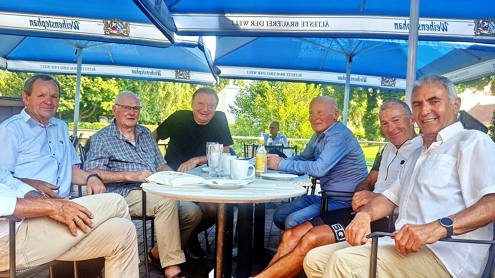 Weitere Gruppe von Gästen sitzt lachend an einem Tisch im Freien