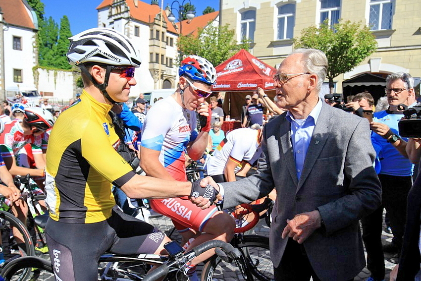Remco Evenepoel im gelben Trikot auf dem Rennrad beim Handschlag mit Gustav-Adolf Schur